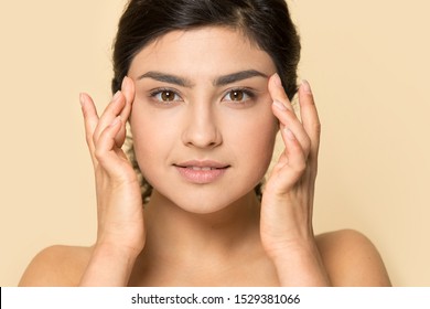 Close Up Headshot Portrait Of Beautiful Indian Millennial Girl Posing On Orange Brown Studio Background Touch Healthy Glowing Skin, Ethnic Young Woman Look At Camera Check Face Mimic Wrinkles