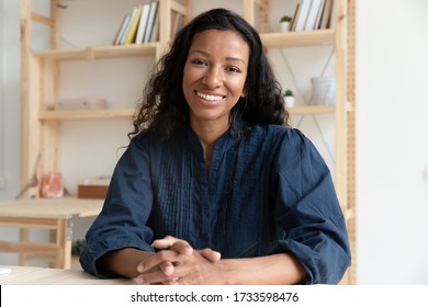 Close Up Headshot Portrait Picture Of Happy African American Businesswoman Sitting By Table. Smiling Attractive Young Diverse Woman Mentor Looking At Camera In Coworking Office.