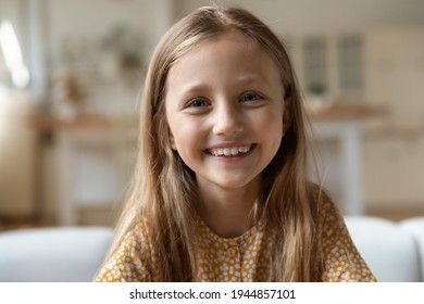 Close up headshot portrait of smiling little 8s Caucasian girl child look at camera talk on video call online. Profile screen view of happy kid have webcam digital conference. Virtual event concept.