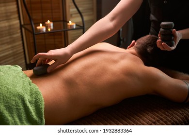 close up healthy man during back stone therapy massage in spa salon, male lying on table relaxing, getting spa therapy