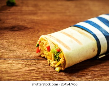 Close Up Of Healthy Vegetarian Couscous Filled Grilled Burrito Wrap With Blue And White Striped Wrapper On Wooden Surface