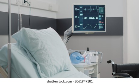 Close Up Of Heart Rate Monitor In Empty Hospital Ward. Nobody In Intensive Care Room With Medical Equipment, Bed, Oxygen Tube And Wheelchair For Recovery. Healthcare Instruments