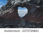 Close up of a heart shape carved out from a volcanic rock arch by the against a beautiful sky with white stratus clouds in Wailuku, Maui, Hawaii, USA