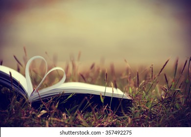 Close up heart shape from paper book on grass field with vintage filter blur background