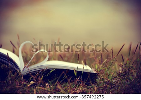 Close up heart shape from paper book on grass field with vintage filter blur background