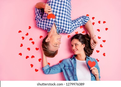 Close up high angle photo of pair in love he him his she her lady boy lying on floor  cuddle to each other with little red paper hearts wearing casual shirts outfit isolated on pale rose background - Powered by Shutterstock