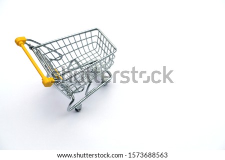 Close up high angle shot selective focus side view an empty miniature metal shopping cart (trolley) with yellow handle on white background. Image of one object with copy space and business concept.