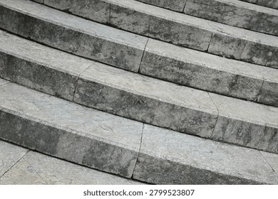 A close up high angle view captures the textured grey stone steps of an old outdoor staircase showing weathering and fine cracks.