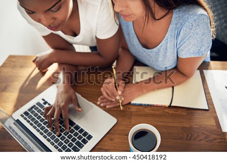 Close up high angle view of two young female business colleagues working on a laptop in a joint startup ebusiness browsing the internet and checking their website