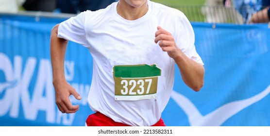 Close up of a high school cross country runner finishing a race wearing a bib on the front of his jersey. - Shutterstock ID 2213582311