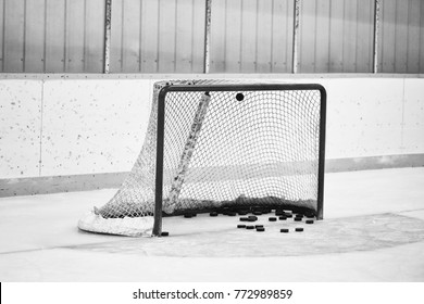 Close Up Of A Hockey Net Full Of Hockey Pucks And Blue Goalie Crease In Front Of Yellow Trimmed Boards