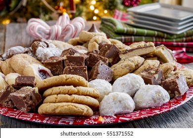 Close Up Of Holiday Cookie Tray Filled With Homemade Cookies And Candy Sitting On Table In Front Christmas Tree With Candy Canes And Plates In Background