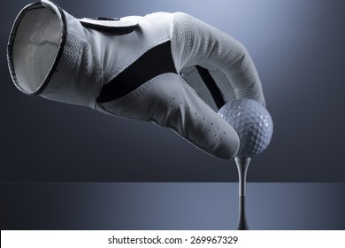 Close Up Of Hollow Golf Glove Putting Ball On Tee, Isolated On Dark Blue Background.