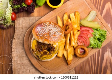 Close up Homemade grilled cheeseburger with fried caramelized onion and melting cheddar cheese serving with finger fries , onion rings , tomato and pickles on wood background. Top view. - Powered by Shutterstock