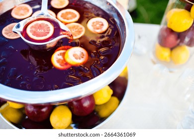 Close up horizontal image of a red punch with yellow lemons on a hot summer day being poured out of a punch bowl with a silver ladle. 