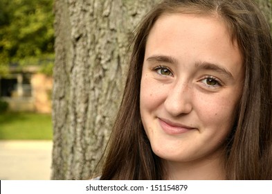 Close Horizontal Portrait Of Female Teen With Closed Mouth Smile Posed In Front Of A Tree