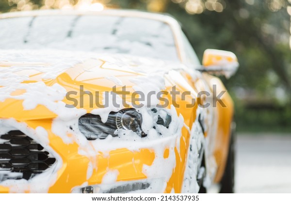 Close up horizontal\
shot of yellow car headlight with cleaning foam, washed at car wash\
service outdoors with high pressure sprayer. Clean car concept. Car\
wash outdoor.