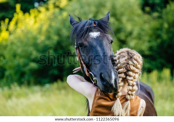 Close up of horse and\
young blonde woman with two braids hugging. People and animals\
friendship concept.