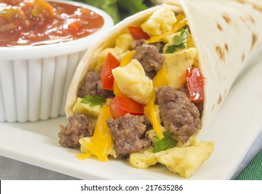 "close up of a hot fresh breakfast burrito with eggs,sausage,cheese,tomatoes,cilantro, and salsa on the side" Breakfast Burrito