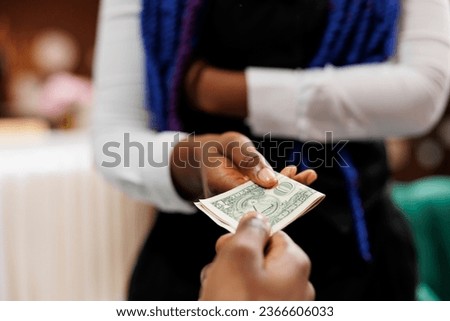 Close up of hotel employee wearing uniform holding money cash taking payment from customer while working in hospitality industry, selective focus. Waitress receiving tip from generous client