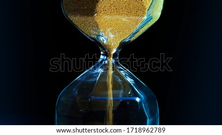 Close up of hourglass with falling golden grains isolated on a dark background. Stock footage. Concept of time, sandglass counting down towards a deadline.