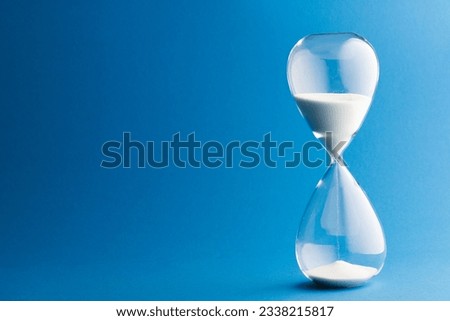 Close up of hourglass with white sand and copy space on blue background. Time, timekeeping, shape and colour concept.
