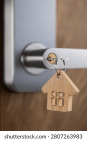 close up of a house key inserted into a modern door lock with a wooden house-shaped keychain. Concept of home ownership, real estate, property investment, apartment purchase, rental housing, mortgage and moving into a new home