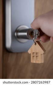 close up of a house key inserted into a modern door lock with a wooden house-shaped keychain. Concept of home ownership, real estate, property investment, apartment purchase, rental housing, mortgage and moving into a new home