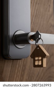 close up of a house key inserted into a modern door lock with a wooden house-shaped keychain. Concept of home ownership, real estate, property investment, apartment purchase, rental housing, mortgage and moving into a new home