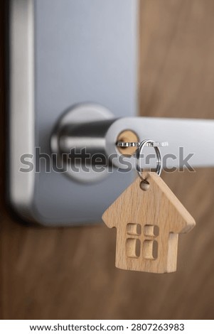 close up of a house key inserted into a modern door lock with a wooden house-shaped keychain. Concept of home ownership, real estate, property investment, apartment purchase, rental housing, mortgage and moving into a new home