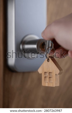close up of a house key inserted into a modern door lock with a wooden house-shaped keychain. Concept of home ownership, real estate, property investment, apartment purchase, rental housing, mortgage and moving into a new home