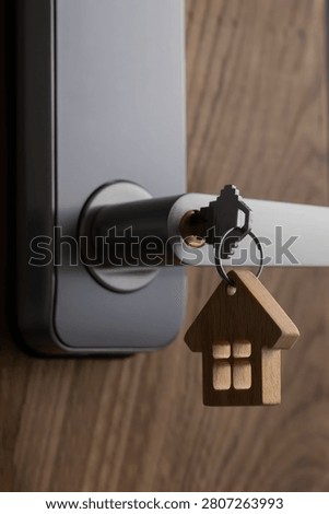 close up of a house key inserted into a modern door lock with a wooden house-shaped keychain. Concept of home ownership, real estate, property investment, apartment purchase, rental housing, mortgage and moving into a new home