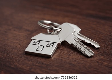 Close up of house keys on a house shaped keychain on wooden background. Concept for real estate, moving home or renting property on dark wood.