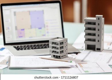 Nahaufnahme eines Hausmodells, das über Wohnungsplänen steht, vor einem Laptop in einem Baubüro. Baubüro-Arbeitskonzept 