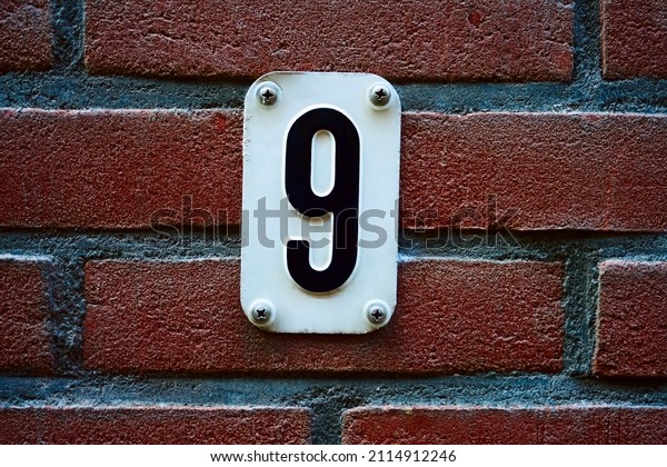 Close Up House Number 9 At Amsterdam The\
Netherlands. House number 9 on red brick wall with number nine on\
white metal plate\
enameled