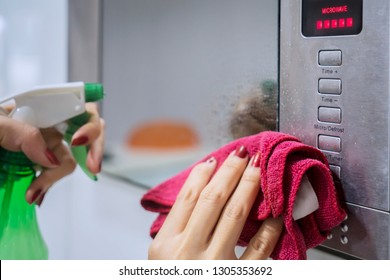 Close Up Of Housemaid Hands Using A Spray Detergent To Clean Microwave In The Kitchen. Shot At Home