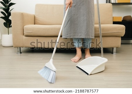 Close up housewife using broom and dustpan wearing an apron to clean the living room at apartment. Young woman is happy to clean home. Maid cleaning service.