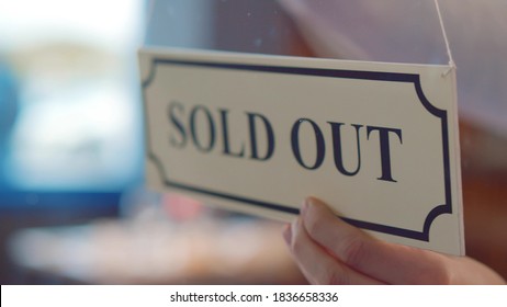 Close Up Of Human Hand Hanging Sold Out Sign On Glass Door Of Cafe Or Store. Owner Putting Sold Out Sign On Window In Local Market Or Bakery Store. Small Business Concept