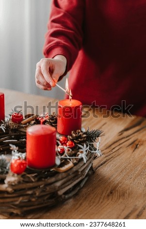 Close up of human hand lighting the first candle on advent wreath. Cozy time before christmas.