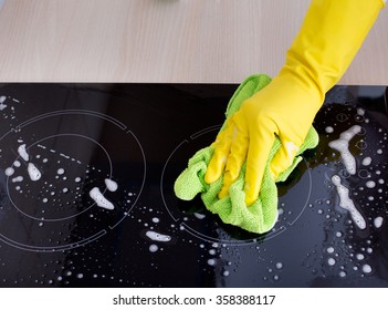 Close up of human hand with protective gloves cleaning induction hob with green mop