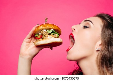 Close Up Of Hungry Girl With Opened Mouth, Holding And Eating Big Hamburger. Pretty Woman With Curly Hairstyle And Red Lips Eating Tasty Cheeseburger With Tomato And Meal. Concept Of Fast Food.