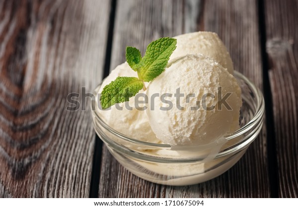Close up of\
ice cream balls with mint leaves in a bowl on a dark wooden rustic\
table. Summer dessert. Selective\
focus