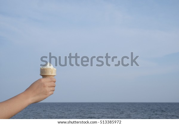 Close up ice cream vanilla cone in woman hand with\
blue sky and sea