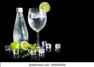 Close up of iced lemon soda in wine glass isolated on black background. Cold homemade lemonade with ice and lemon. Bottles of sparkling, soda, drinking water, natural mineral water and ice cubes - Shutterstock ID 1096325966
