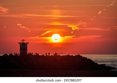 Close up the iconic red-white striped harbor light of Northern Pier and silhouette of people enjoying the sun setting in the North Sea from the beach of Scheveningen, the Netherlands