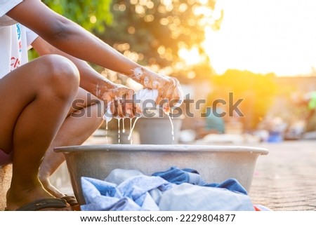 close up image of african squeezing a wet material, basin in front- golden hour image of unidentified black person washing outdoor 