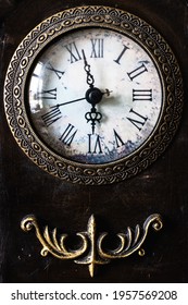 Close Up Image Of An Antique Clock Face And Metal Decoration Below On A Dark Background. The Time Shows A Few Minutes Before 6 And Includes A Seconds Hand.