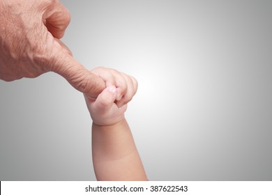 Close up image of baby's hand holding elderly's finger