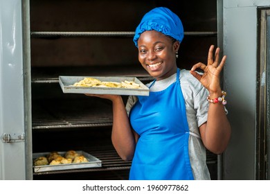 close up image of beautiful african lady in front of a local oven- cheerful black woman in apron and a head wrap with cookies - baking concept
