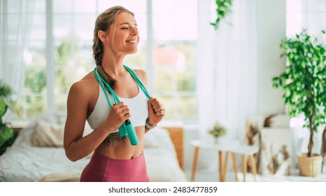 Close up image of beautiful happy excited young sporty slim woman carrying jumping rope on shoulders after home workout and looking away. Sport and recreation concept at home. Strong and power - Powered by Shutterstock